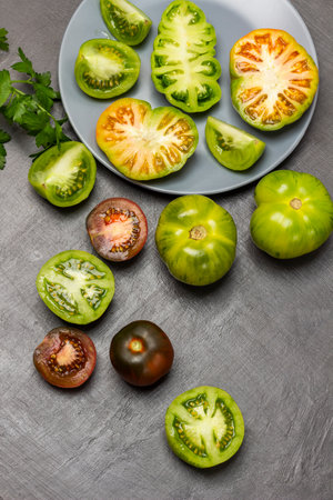 Different varieties of green and red tomatoes in a plate and on the table. flat lay. gray background.の写真素材