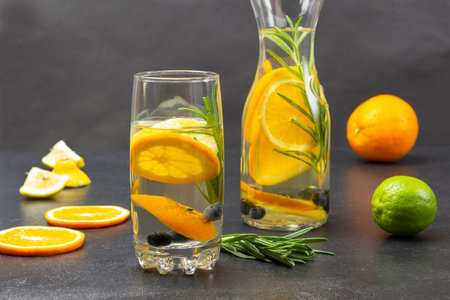 Sliced orange slices and rosemary sprig on table. Infused summer drink with oranges, blueberries and rosemary in glass and bottle. Orange and lime on table. black backgroundの写真素材