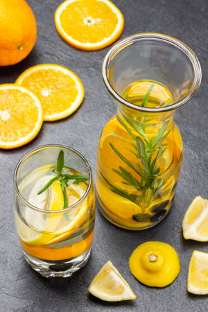 Infused summer drink with oranges, blueberries and rosemary in glass and bottle. Sliced orange slices on table. top view. black backgroundの写真素材