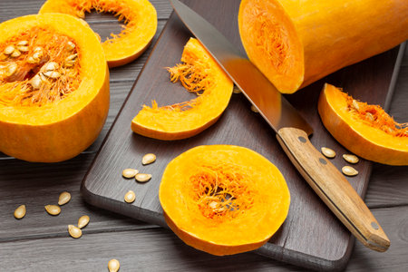 Knife, pumpkin slices on cutting board. Half a pumpkin on the table. top view. Dark wooden background.の写真素材