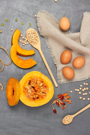 Eggs on napkin. Sliced pumpkin pieces and half pumpkin. Chickpeas in wooden spoon. flat lay. gray background.の写真素材