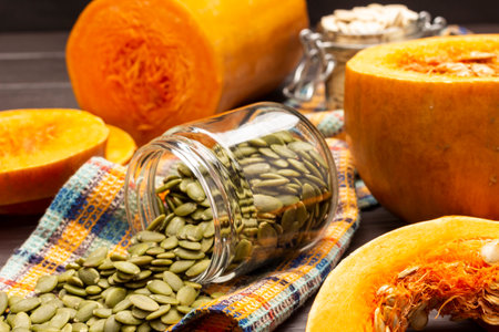 Peeled pumpkin seeds in glass jar. Half pumpkin on table. close up. top view.の写真素材