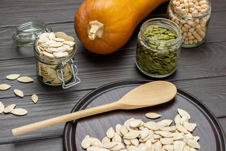 Pumpkin seeds in glass jars. Wooden spoon and seeds on board. top view. dark wooden backgroundの写真素材