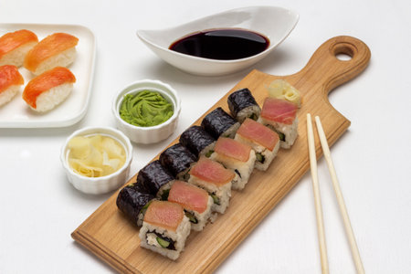 Nori maki, sushi with salmon and tuna on cutting board. Soy sauce in bowl, ginger and wasabi. top view. white backgroundの写真素材