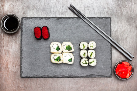 Sushi rolls and chopsticks on stone board. Ginger and soy sauce in bowls. flat lay. dark brown backgroundの写真素材