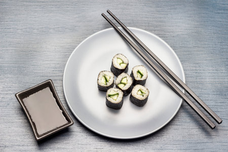 Sushi nori rolls and chopsticks on blue plate. Sauce boat in black bowl. flat lay. copyspace. blue backgroundの写真素材
