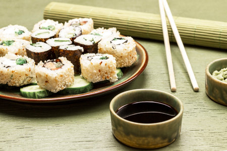 Sushi set with cucumbers on green plate. Soy sauce in bowls. Bamboo mat and chopsticks. top view. green backgroundの写真素材