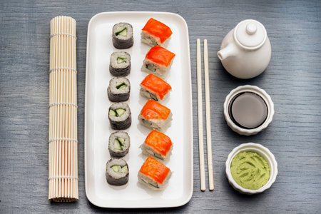 Sushi set on white plate. Soy sauce and wasabi in bowls. Bamboo mat and chopsticks. flat lay. blue backgroundの写真素材