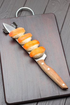 Sushi with salmon on knife blade and on cutting board. copyspace. top view. dark wooden backgroundの写真素材