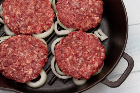 Raw beef burgers with chopped onions in frying pan. top view. white backgroundの写真素材