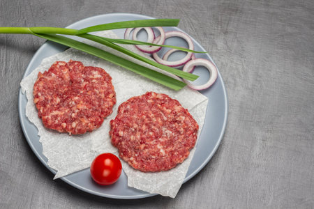 Two raw beef burgers with green onion and tomato on gray plate. copyspace. top view. brown background.の写真素材
