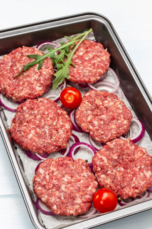 Raw beef burgers with chopped onions and tomatoes on baking tray. top view. white backgroundの写真素材