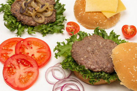 Fried burger bun on lettuce leaf, fried burger with cheese and fried onions, chopped tomatoes and onions. flat lay. white backgroundの写真素材