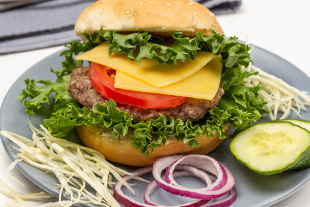 Burger bun on lettuce leaf with cheese and tomatoes, chopped cucumber and onions on gray plate. top view. white backgroundの写真素材
