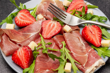 Spanish jamon with strawberries and arugula on gray plate. close up. top view. black backgroundの写真素材