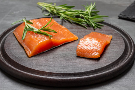 Pieces of salmon and sprigs of rosemary on cutting board. close up. brown backgroundの写真素材