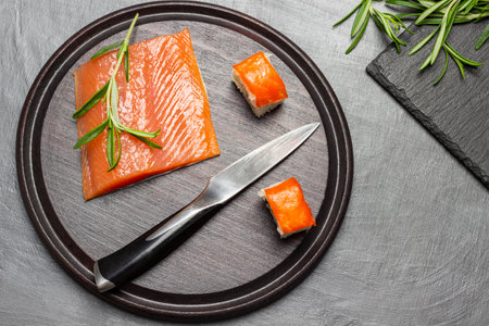 Pieces of salmon, kitchen knife and sprigs of rosemary on cutting board. flat lay. brown backgroundの写真素材