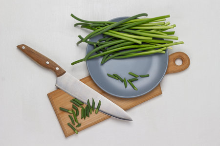 Green pods of garlic on gray plate. Cutting pods of garlic and knife on cutting board. copyspace. top view. white background.の写真素材