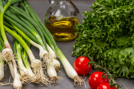 Green onions with roots, lettuce, tomatoes and a bottle of olive oil. gray background. top viewの写真素材
