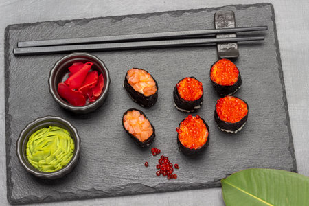 Ginger and wasabi in black bowls. Nori sushi with caviar and salmon. Black chopsticks. stone board. flat lay. gray backgroundの写真素材