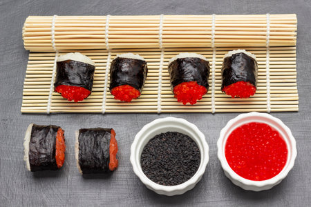 Sushi nori rolls with caviar and salmon on bamboo mat and on table. Black sesame and caviar in white bowls. top view. gray background.の写真素材