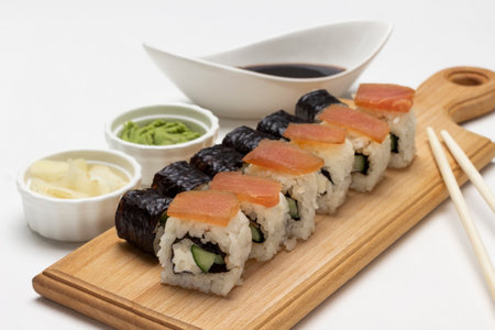 Sushi nori and sushi rolls with salmon on the board. Soy sauce, ginger and wasabi in bowls. top view. white backgroundの写真素材