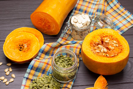 Pumpkin seeds in glass jars. Half pumpkin and sliced pieces of pumpkin on napkin. top view. Dark wooden background.の写真素材