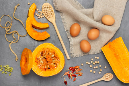 Eggs on napkin. Sliced pumpkin pieces and half pumpkin. Chickpeas in wooden spoon. flat lay. gray background.の写真素材