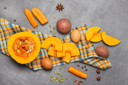 Half pumpkin and sliced pieces of pumpkin on napkin. Potatoes and carrots on table. flat lay. gray background.の写真素材