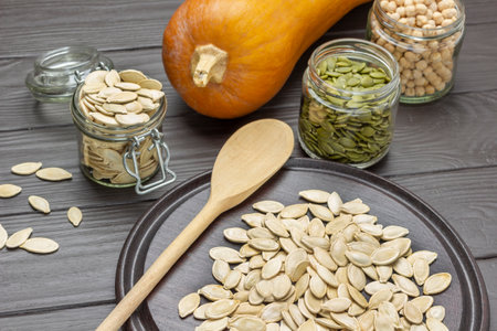 Pumpkin seeds in glass jars. Wooden spoon and seeds on board. top view. dark wooden backgroundの写真素材