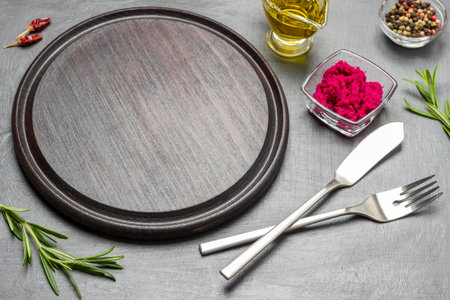 Empty cutting board, knife and fork. Allspice and horseradish in glass bowl on table. top view. black backgroundの写真素材