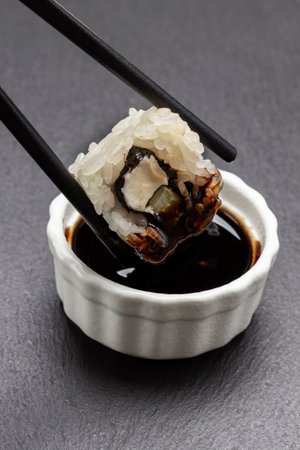 Chopsticks hold sushi and dunk in sauce. Black background.の写真素材