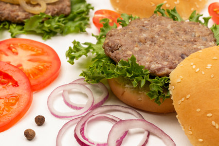 Burger bun on lettuce leaf. Chopped tomatoes and onions on table. top view. white backgroundの写真素材