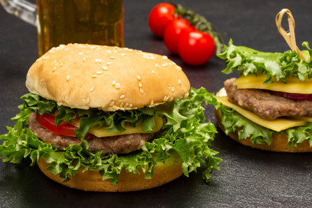 Cheeseburger with greens on bun with sesame seeds. Branch of tomato on the table. top view. black backgroundの写真素材