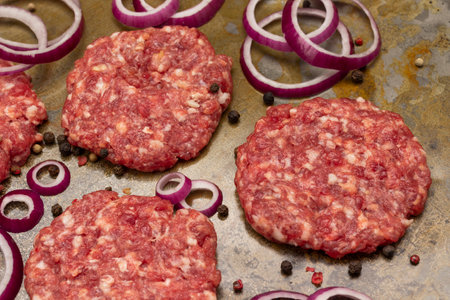 Raw beef burgers with chopped onions and allspice on baking tray. close up. top viewの写真素材