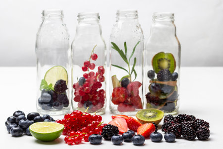 Red currants, strawberries, blueberries and blackberries on table. Glass bottles with berries. white backgroundの写真素材