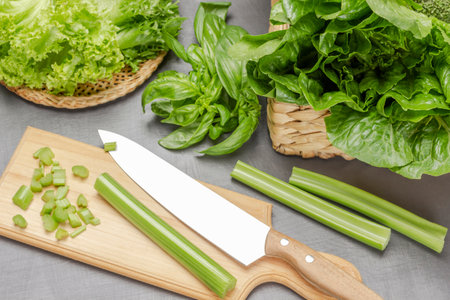 Knife and celery stalks on cutting board. Lettuce leaves in wicker basket and plate. top view. gray background.の写真素材
