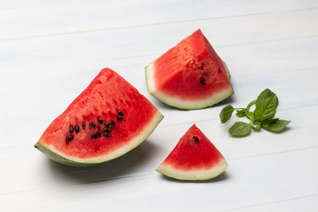 Pieces of watermelon and a sprig of basil. copyspace. top view. White wood background.の写真素材
