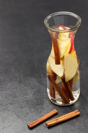 Cinnamon and apple infused water in a glass bottle. Cinnamon sticks on table. copyspace. Black background. top viewの写真素材