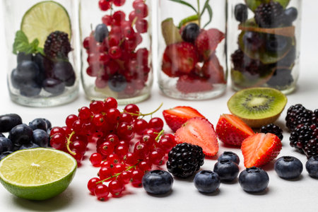Red currants, strawberries, blueberries and blackberries on table. Glass bottles with berries. close up. white backgroundの写真素材