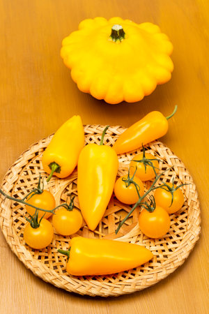Yellow peppers and tomatoes on wicker plate. Yellow patisson on table. top view. yellow background.の写真素材