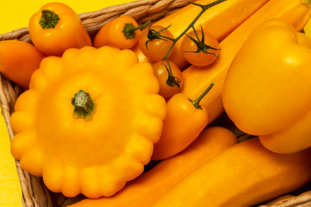 Set of yellow vegetables on wicker basket: patissons, peppers and tomatoes on branch. flat lay. yellow background.の写真素材