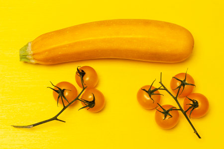 Yellow zucchini and two sprigs of yellow tomatoes. flat lay. yellow backgroundの写真素材