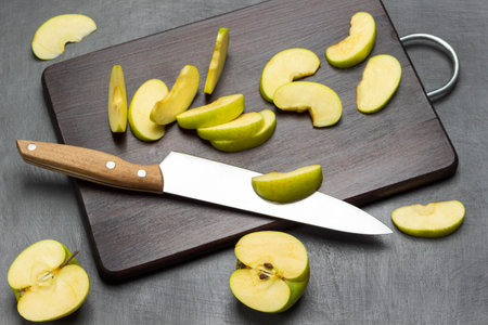 Two halves of green apple. Kitchen knife and apple slices on cutting board. flat lay. gray background.の写真素材