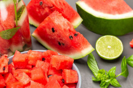 Sliced watermelon pulp in bowl. Slices of watermelon, half a lime and sprig of basil on table. close up. gray background.の写真素材