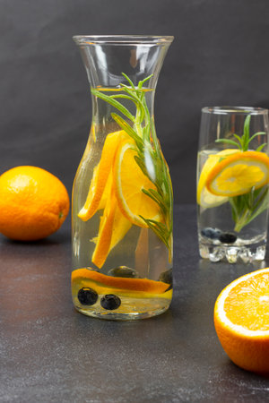 Infused summer drink with oranges, blueberries and rosemary in bottle. orange table. black backgroundの写真素材