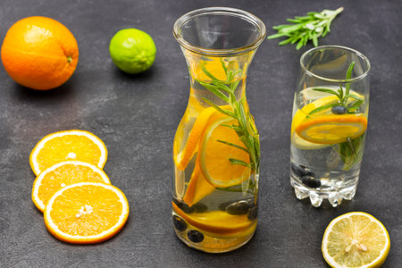 Orange, blueberries and rosemary infused water in glass and bottle. Orange and lime on table. black backgroundの写真素材