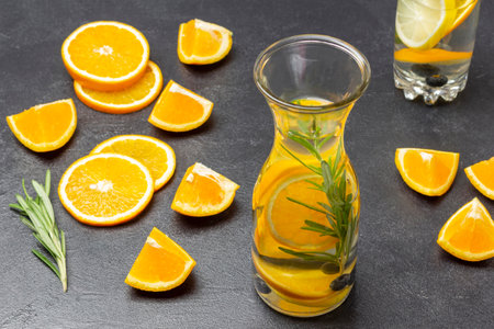 Infused summer drink with oranges, blueberries and rosemary in bottle. Sliced orange slices and rosemary sprig on table. black backgroundの写真素材