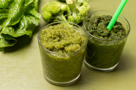 Green smoothie in two glasses. Broccoli and lettuce on table. close up. top view. green background.の写真素材