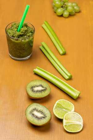 Green smoothie in glass. Lime and kiwi halves, celery stalks and grapes on table. top view. mustard color background.の写真素材